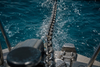 Wet anchor chain being hauled up over a boat's bow from turquoise water