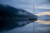 A yacht sitting at anchor on calm, glassy water at dawn