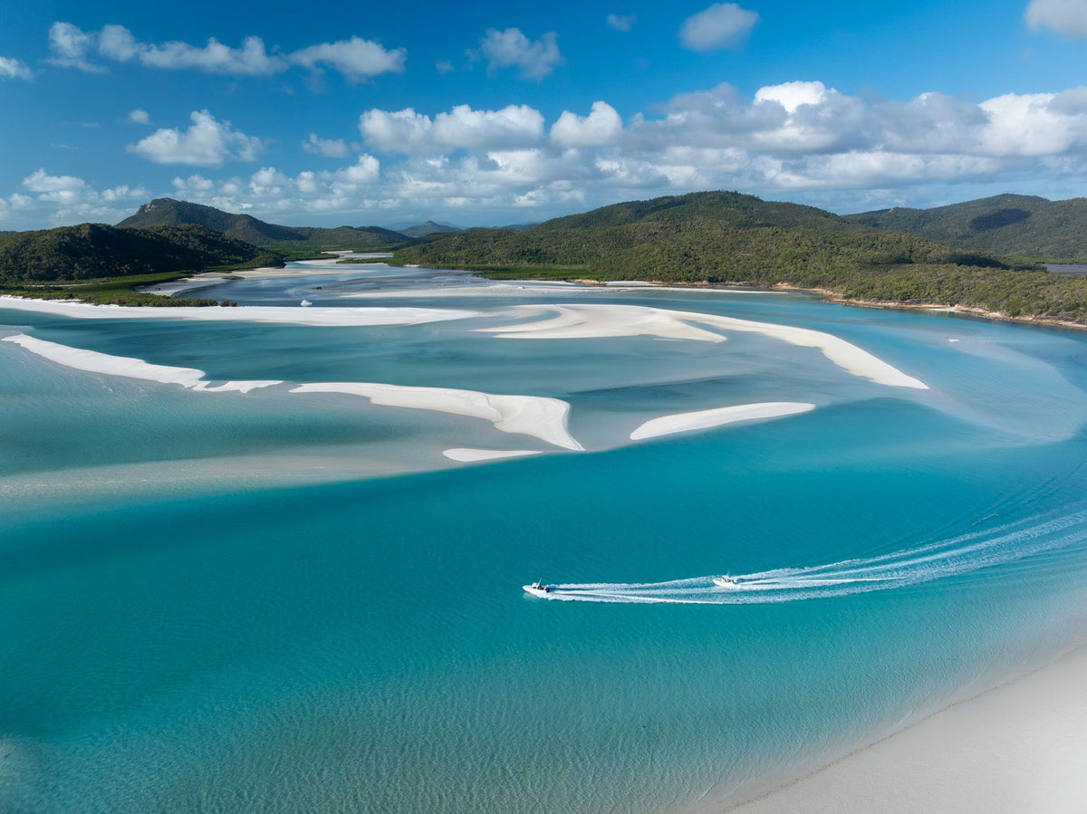 Aerial view of two boats cruising across turquoise water past white sand swirls in the Whitsundays