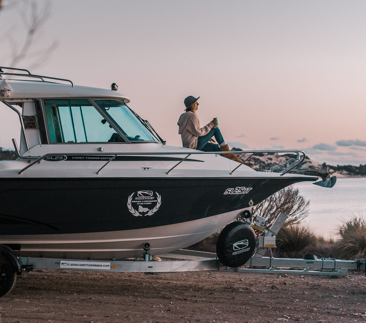 Two boaters sitting on the bow of a moored trailer boat at a marina, with a Savwinch drum anchor winch and bowsprit fitted