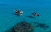 Aerial view of two fishing boats anchored in clear turquoise water beside a reef, with snorkellers swimming nearby