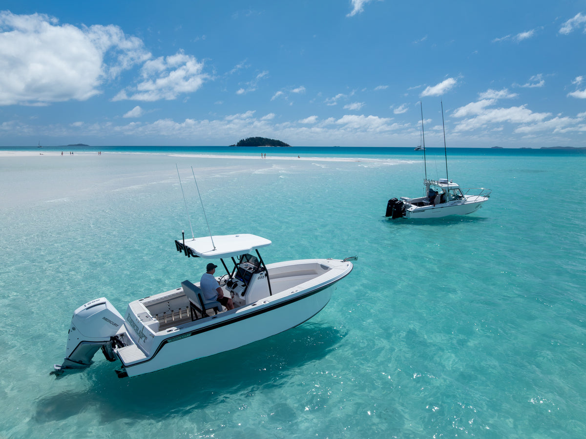 Centre console and hardtop fishing boats anchored in shallow turquoise water off a white sand beach in the Whitsundays